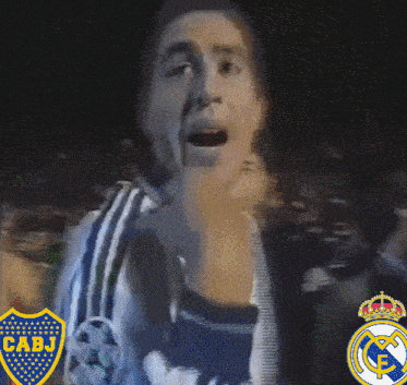 a man wearing a cabj shirt stands in front of a real madrid logo