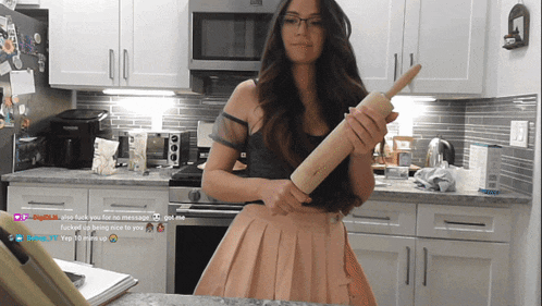 a woman holding a rolling pin in a kitchen with a screenshot of a twitch stream