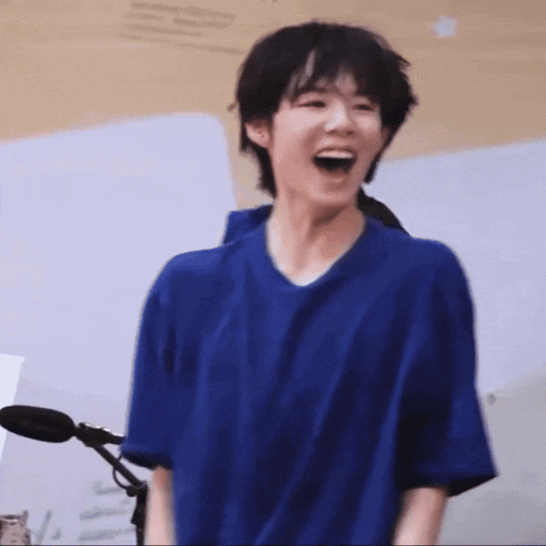 a young man in a blue shirt is laughing in front of a microphone