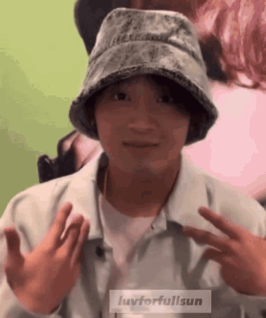 a man wearing a bucket hat is making a peace sign .