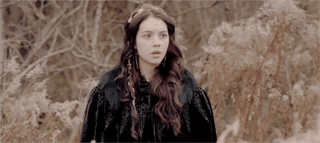 a woman wearing a black cape and a crown is standing in a field
