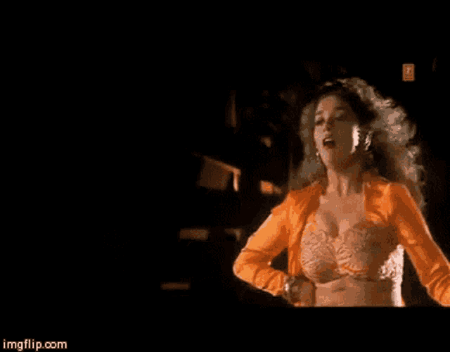 a woman in a bra and orange jacket is dancing in a dark room ..