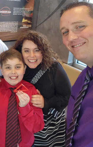 a man in a purple tie stands next to a woman and a boy in front of a mcdonald 's sign