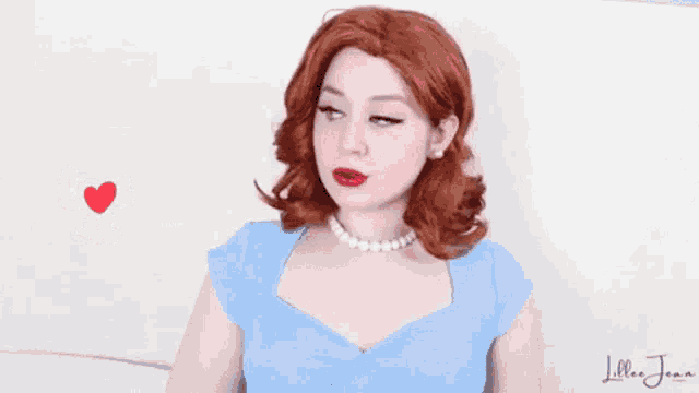a woman wearing a blue dress and a pearl necklace has a red heart behind her and the name lillie jean