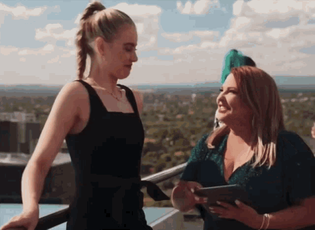 two women are standing next to each other on a balcony looking at a tablet