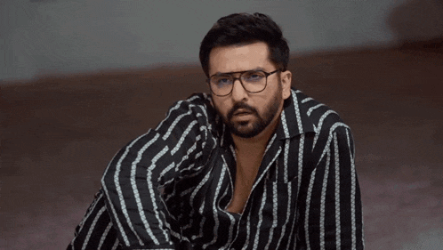 a man wearing glasses and a striped shirt is sitting on the floor