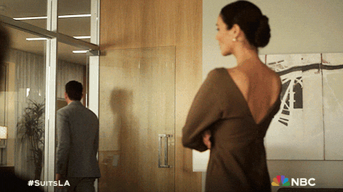 a woman in a brown dress is standing in front of a man in a suit and the nbc logo is on the bottom