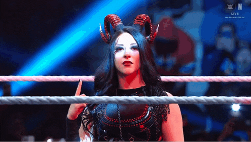 a woman with horns is standing in a wrestling ring and giving the middle finger