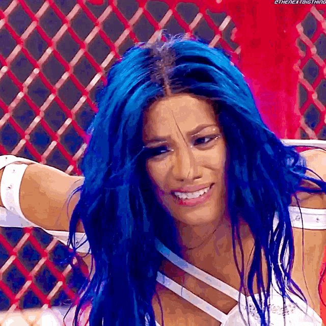 a woman with blue hair is smiling in front of a red fence