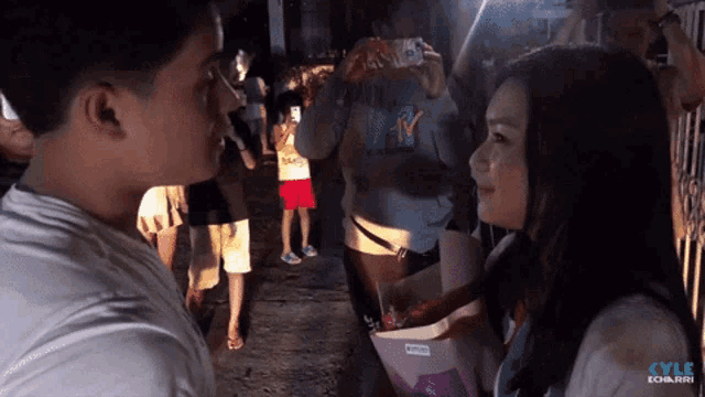 a man taking a picture of a woman with a phone with kyle ebarra written on the bottom