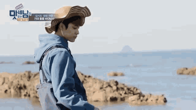 a man wearing a hat is standing on a rocky beach .