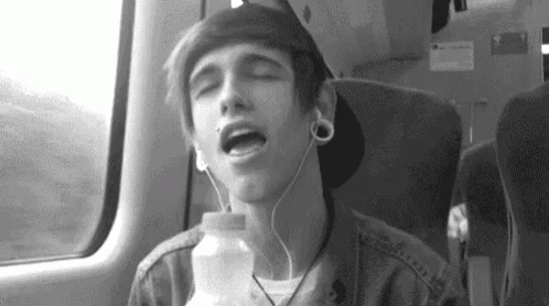 a young man is sitting on a train wearing headphones and holding a bottle .