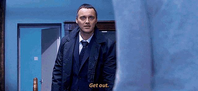 a man in a suit and tie is standing in a room and says get out