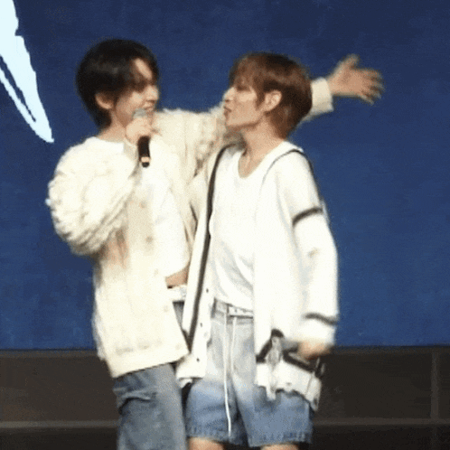 a couple of men are standing next to each other on a stage and one of them is holding a microphone .