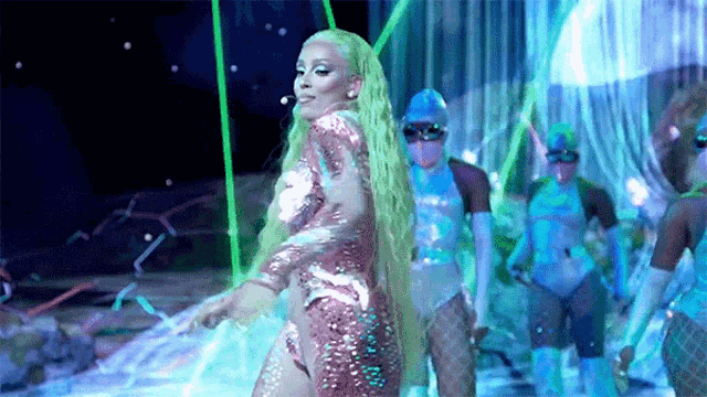 a woman with long green hair is dancing on a stage in front of a group of people .