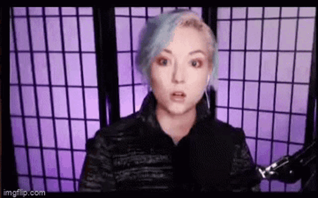 a woman with blue hair is standing in front of a purple curtain .