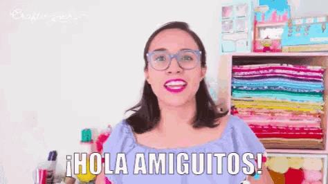 a woman wearing glasses and purple lipstick says hola amiguitos
