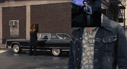 a man in a denim jacket stands in front of a car with a picture of a man in a tuxedo behind him