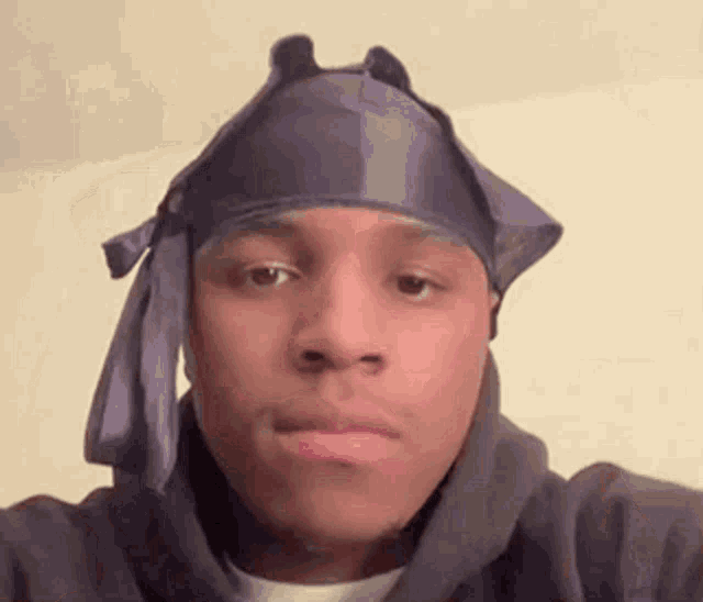 a young man wearing a purple headband and a hoodie is looking at the camera .