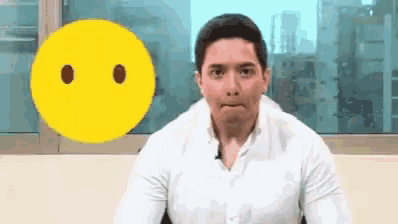 a man in a white shirt is making a face in front of a yellow smiley face .