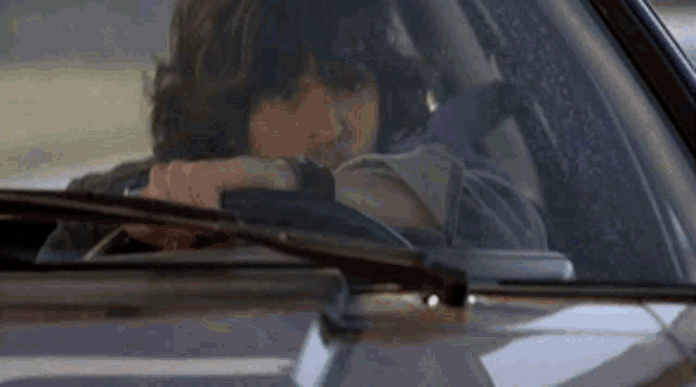 a man is sitting in a car looking out the window .