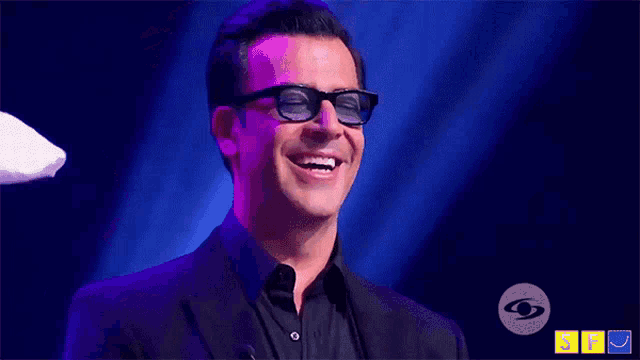 a man wearing glasses and a black shirt is smiling in front of a blue background