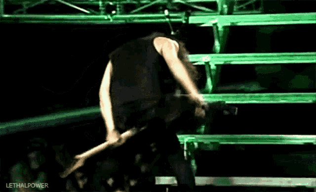 a man in a black tank top is doing a handstand in front of a green fence .