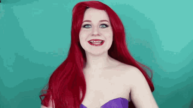a woman with red hair is wearing a little mermaid costume and smiling .