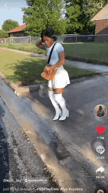 a woman in a white skirt and white boots stands on a sidewalk