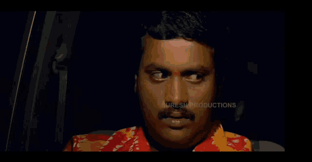 a man in a red shirt is sitting in the back seat of a car with suresh productions written on the bottom