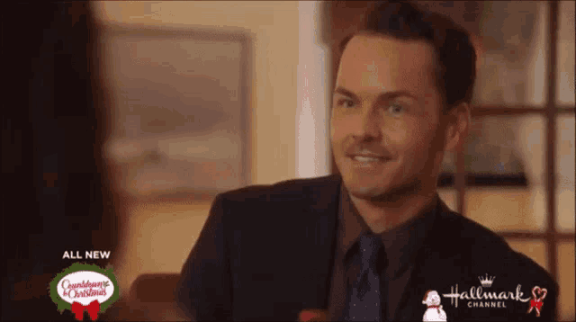 a man in a suit and tie is smiling in front of a sign for hallmark channel