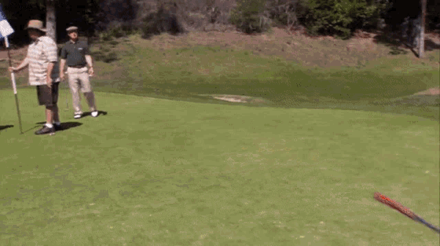 a group of men are playing golf on a green with a flag in the background