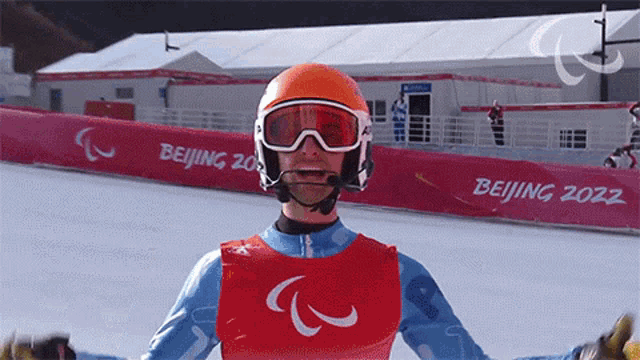 a man wearing a helmet and goggles stands in front of beijing 2022 banners