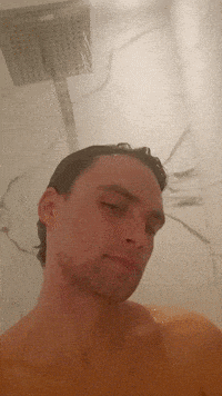 a man taking a shower with his eyes closed and a shower head in the background