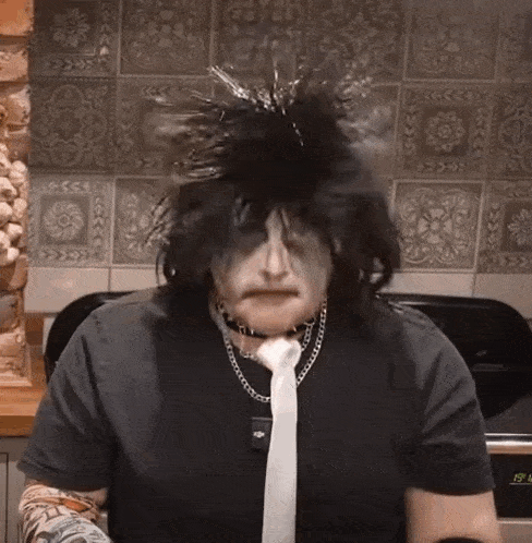 a man wearing a black shirt and a white tie is sitting in front of a stove with the time of 19:58