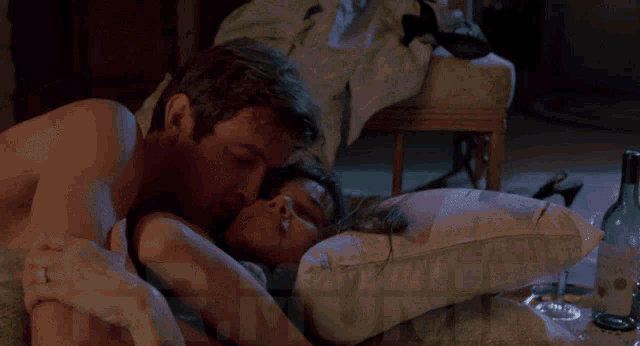 a man kissing a woman on a pillow in a room with a bottle of wine in the background