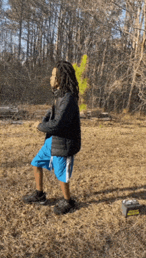 a man with dreadlocks is standing in a field next to a battery that says ' aa ' on it