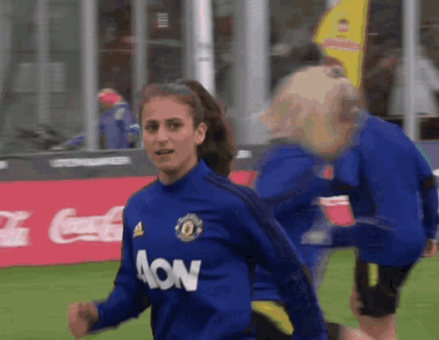a woman wearing a blue aon jersey runs on a soccer field