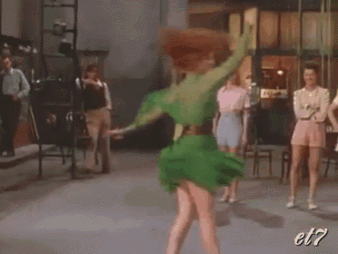 a woman in a green dress is dancing in front of a group of people with the letters et7 on the bottom