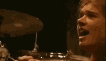 a man is sitting in front of a drum set and talking on a cell phone .