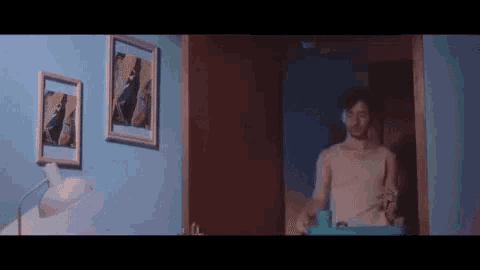 a man without a shirt is standing in a hallway holding a tray with flowers on it .