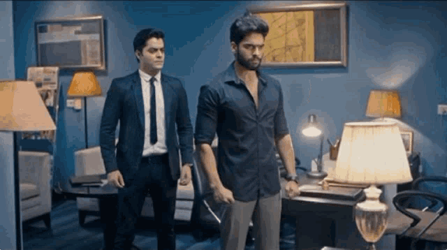 two men in suits and ties are standing next to each other in a living room