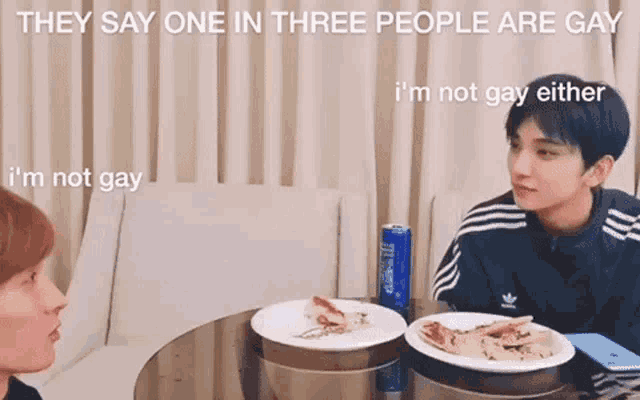 two men are sitting at a table with plates of food and talking .