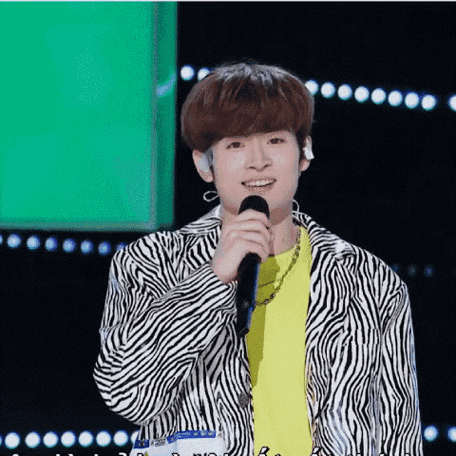 a young man wearing a zebra print jacket is holding a microphone and smiling