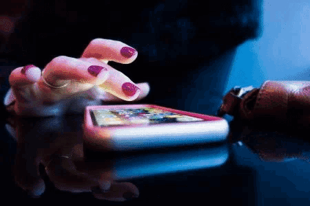 a woman 's hand with red nail polish is using a cell phone