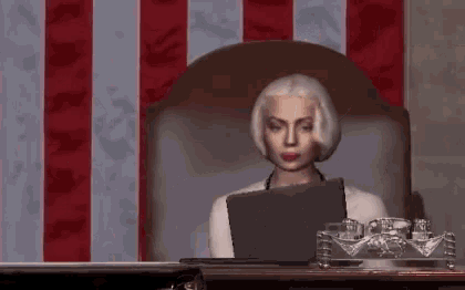 a woman sitting in front of an american flag looking at a laptop
