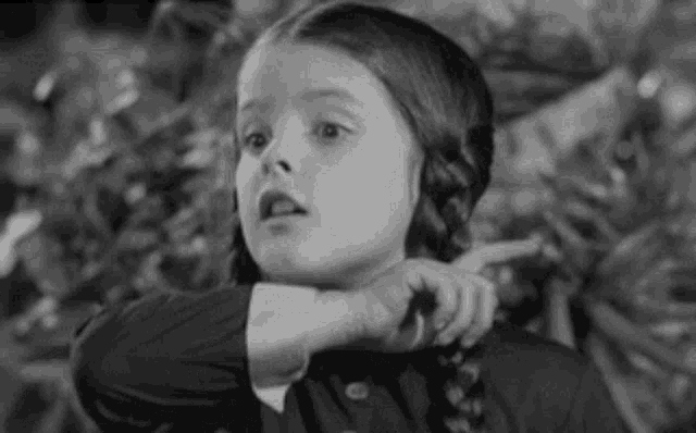 a little girl in a black and white photo is pointing at something .