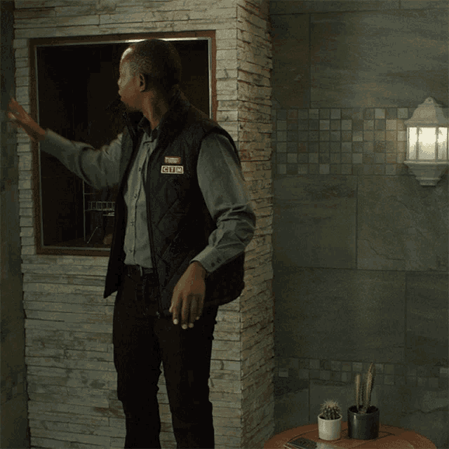 a man wearing a vest that says security stands in front of a brick wall