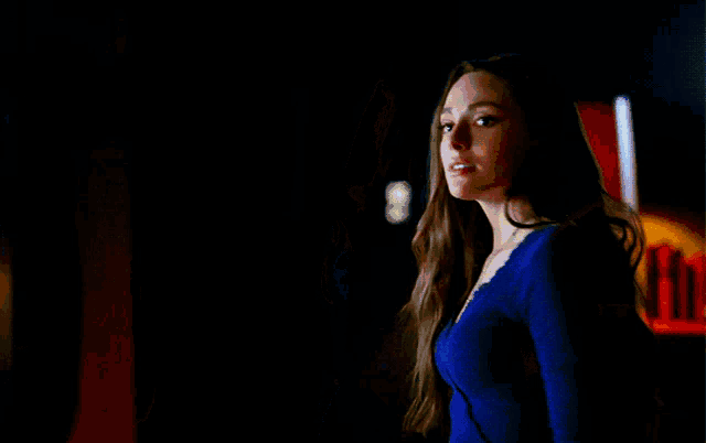 a woman in a blue shirt is standing in a dark room with a lamp