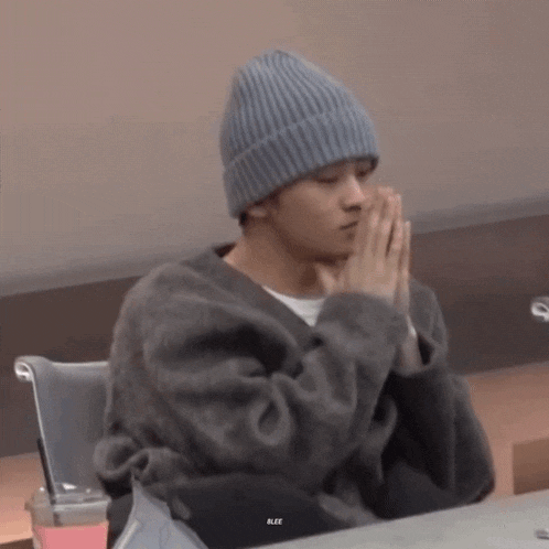 a man wearing a beanie and a sweater is praying with his hands folded .